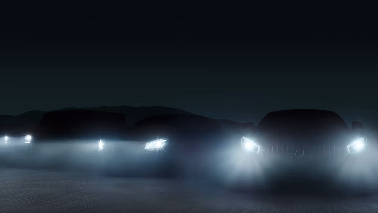 Frontscheinwerfer von aufgereihten Mercedes-AMG Fahrzeugen scheinen im dunklen durch den Nebel