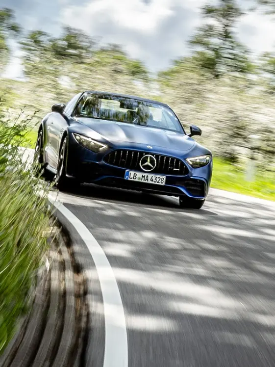 A dark Mercedes-AMG drives on a curved country road towards the viewer