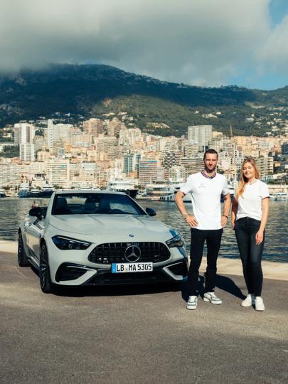 Maro Engel und Sabrine Berchtold posieren mit dem neuen Mercedes-AMG CLE 53 4MATIC+ Cabriolet vor einer Hafenstadt