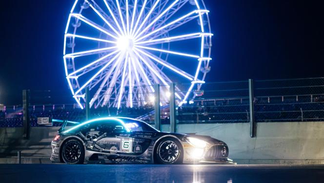 A Mercedes-AMG GT racing car is parked at night in front of an illuminated Ferris wheel
