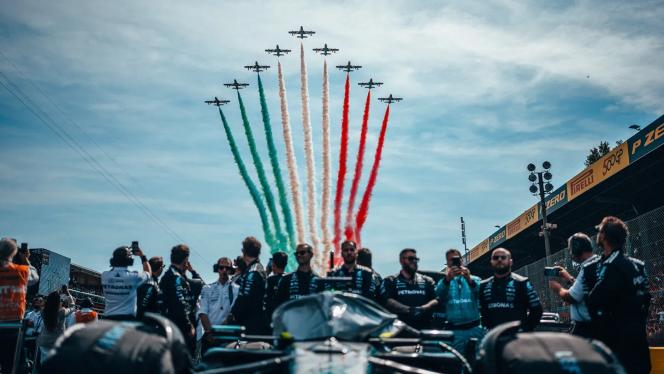 The Mercedes-AMG PETRONAS F1 Team stands on the track at Monza while a formation of aeroplanes sprays the Italian national colours across the sky.