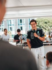 George Russell steht lachend mit einem Mikrofon in der Hand vor einem Bartresen.