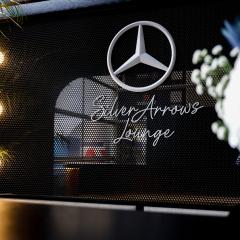 Unterhalb eines weißen Mercedes-Sterns an einer schwarzen Metallwand befindet sich der Schriftzug „Silver Arrows Lounge“