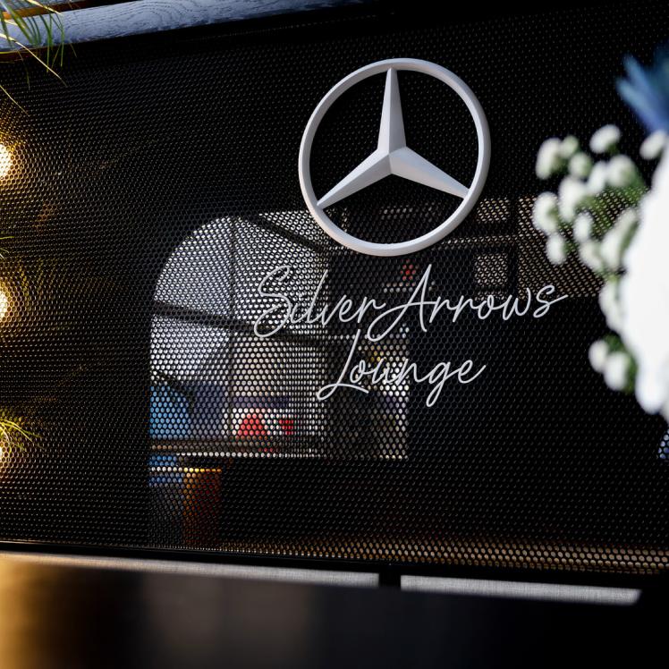 Unterhalb eines weißen Mercedes-Sterns an einer schwarzen Metallwand befindet sich der Schriftzug „Silver Arrows Lounge“